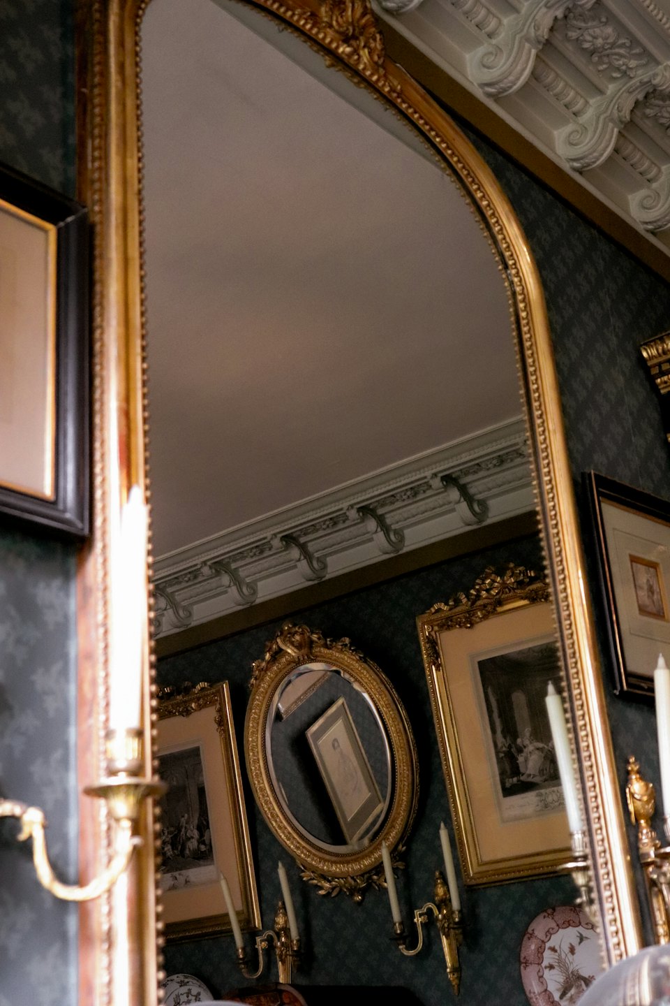 Gold framed mirror reflecting a ceiling against patterned wallpaper.