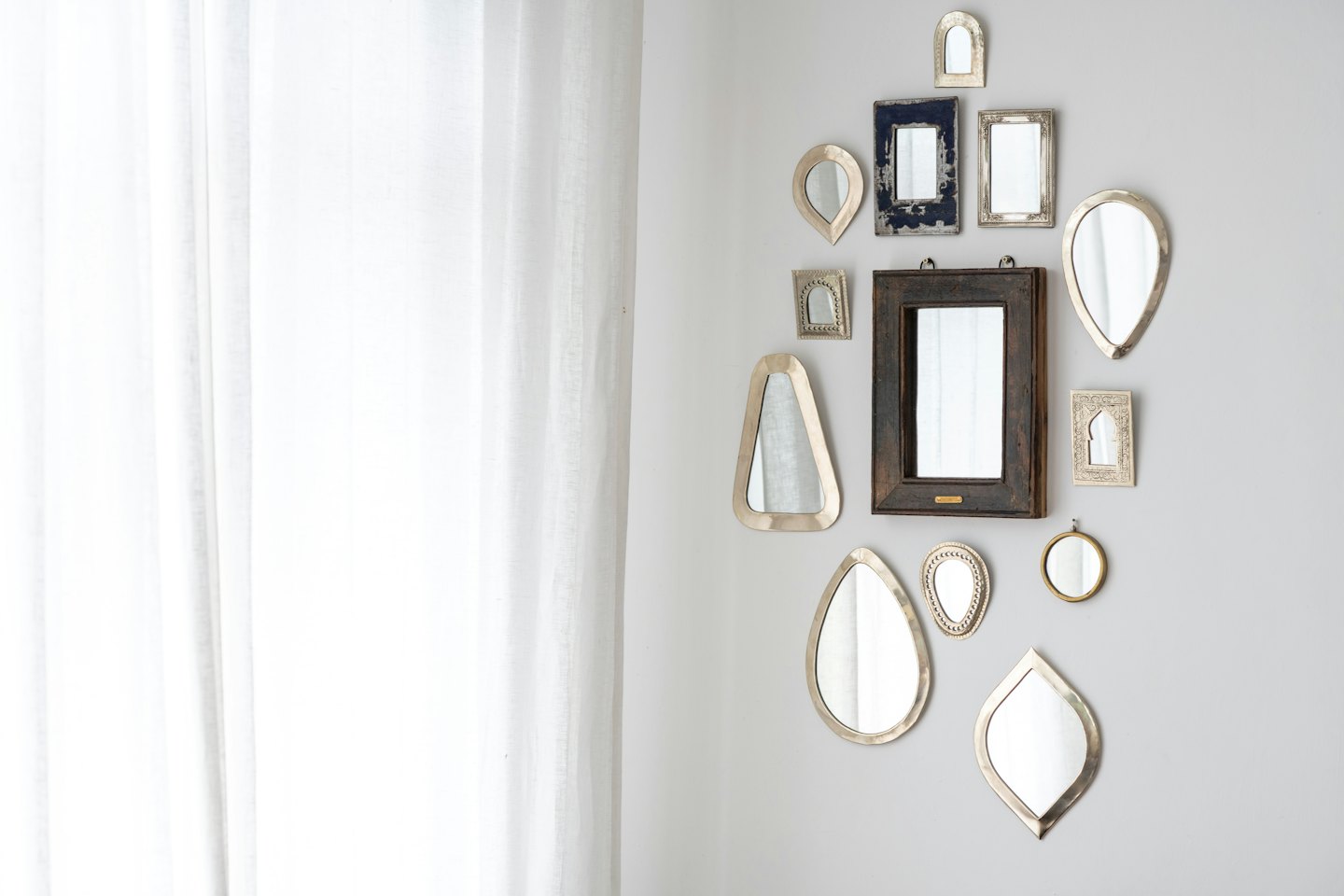 Gallery wall of eclectic decorative mirrors on grey wall.
