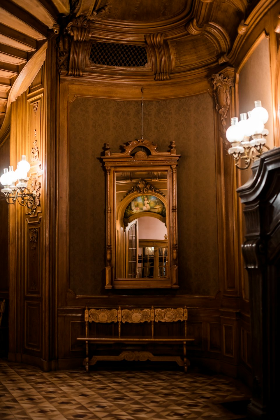 An ornate wooden bench sits below a large carved mirror.