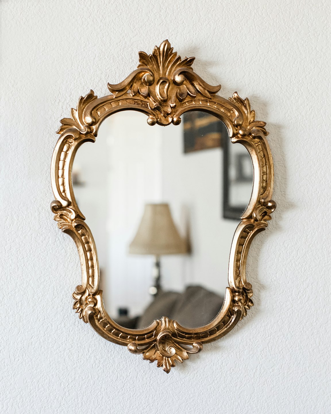 Ornate gold mirror hangs on a textured white wall.