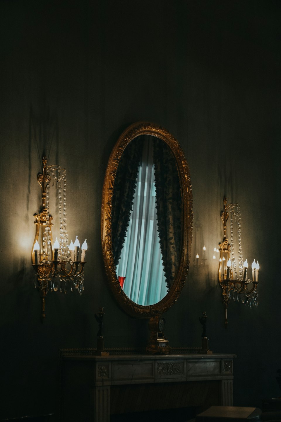 Ornate gold mirror and wall sconces above a marble console.