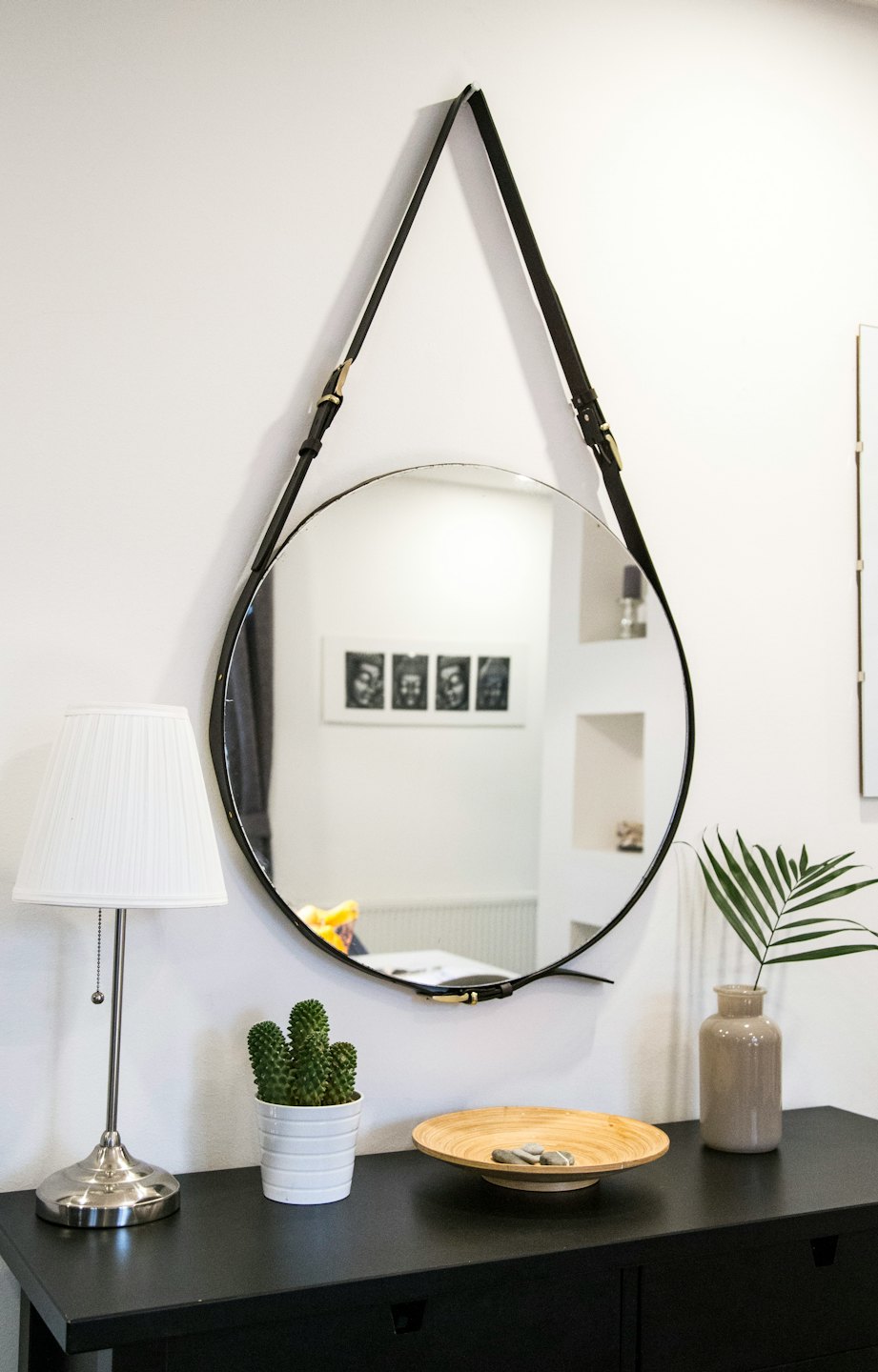 Round mirror with leather strap above console table with decor.